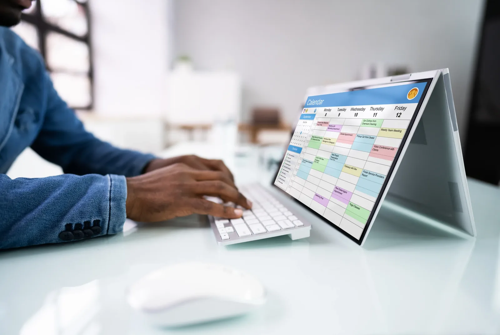 A person working at a desk with a calendar displayed on a laptop screen.